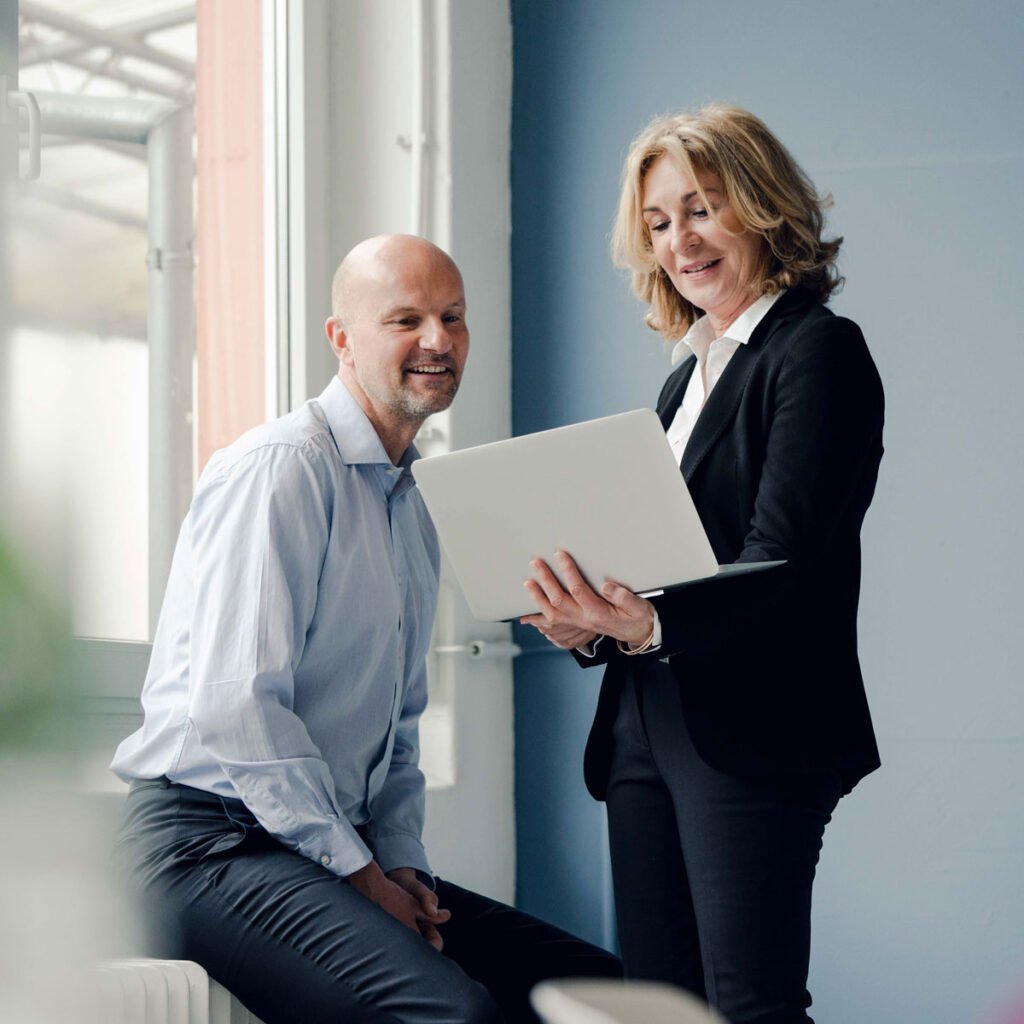 Two business professionals collaborating on a laptop in a modern office setting, showcasing teamwork and innovation by D&E Decor.