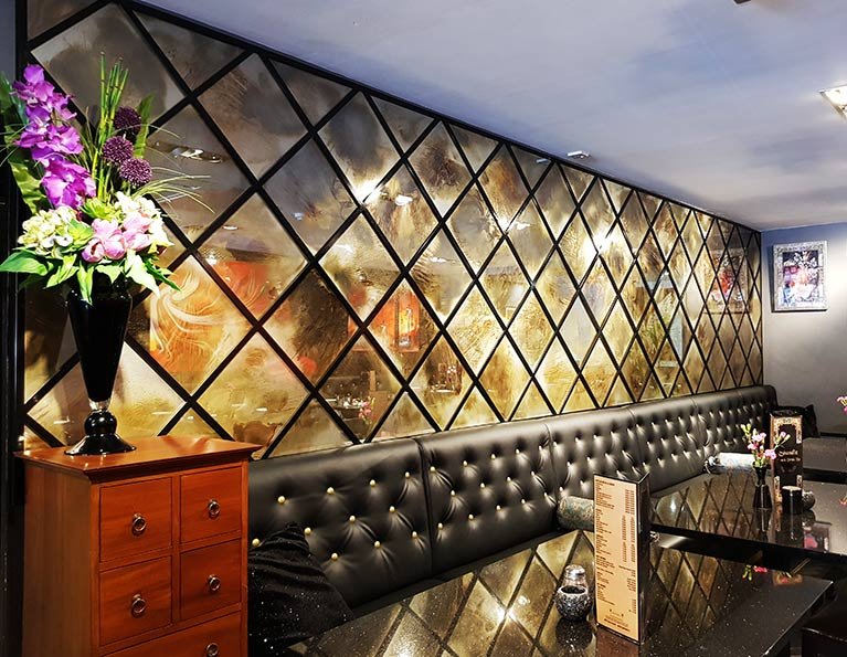 Antique mirrored glass feature wall with diamond patterns in a Persian restaurant, complementing luxurious black seating and elegant floral decor